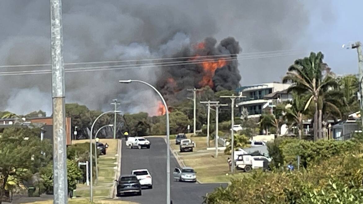 Police cars shut down the street as flames crown above the tree line. Picture by James Parker