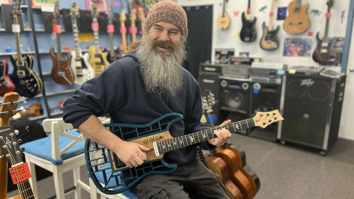 Nate Hughston provides a cheeky smile while playing the custom Traveler guitar at his store on Auckland Street in Bega. Picture by James Parker