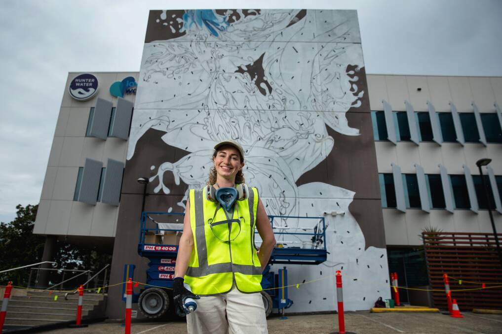 Artist Rosie Woods in front of the mural she is painting on Hunter Water's headquarters on Honeysuckle Drive. Picture by Marina Neil