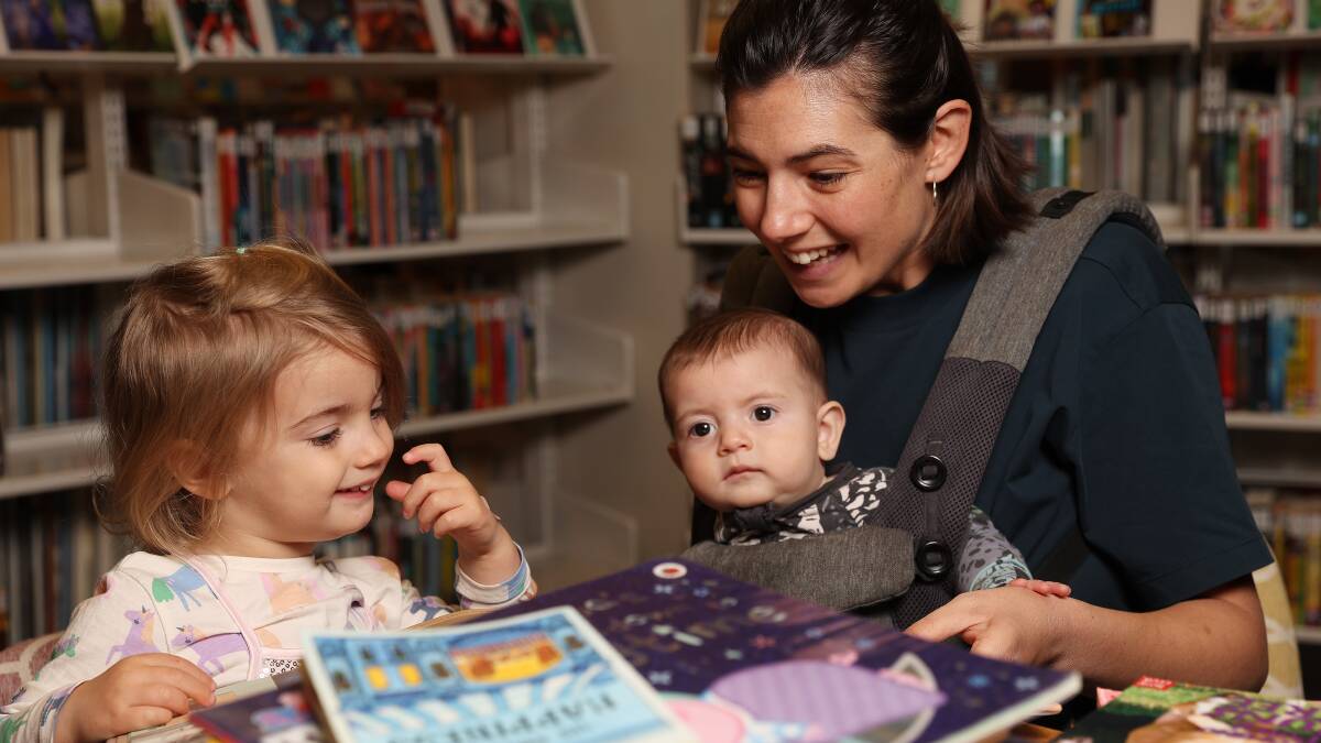 Saskia Bullock, 2, reads a book at Wallsend library with mum Gemma Wolk and brother Orson Bullock, 4 months. Picture by Peter Lorimer